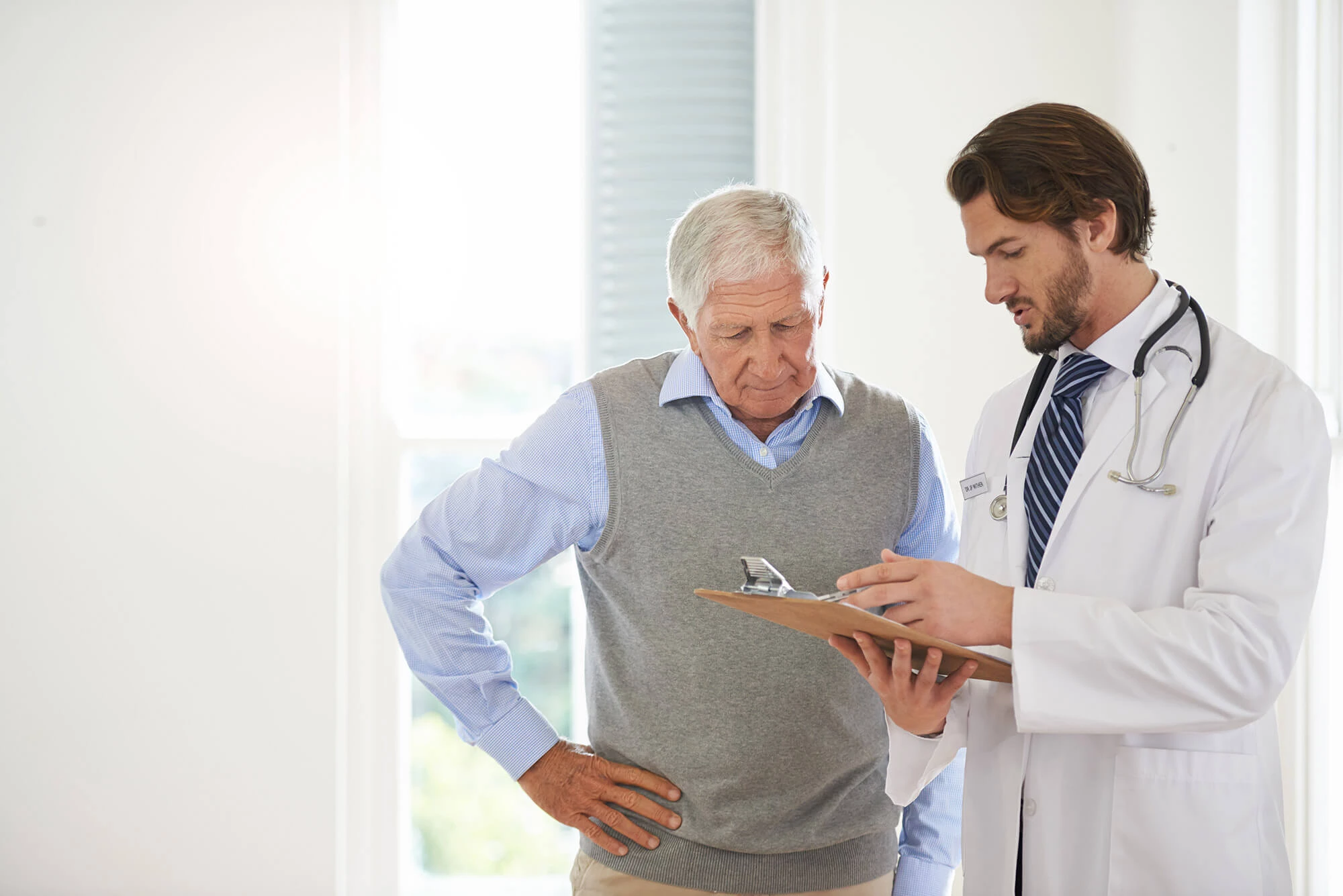 A male doctor showing an older man a chart on a clipboard.