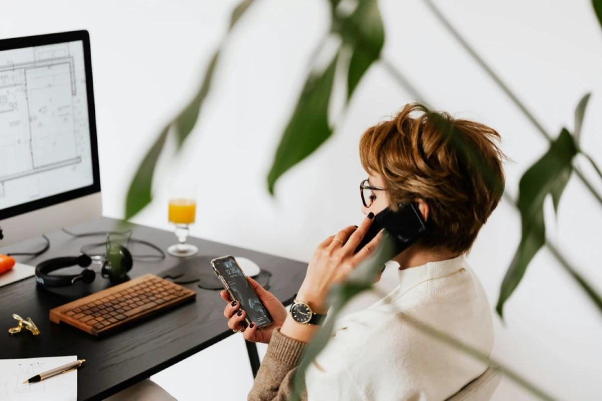 woman on the phone looking at her smart phone in front of her computer