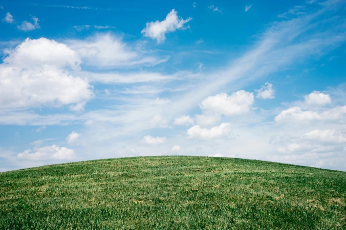 green round hill with blue sky and white clouds