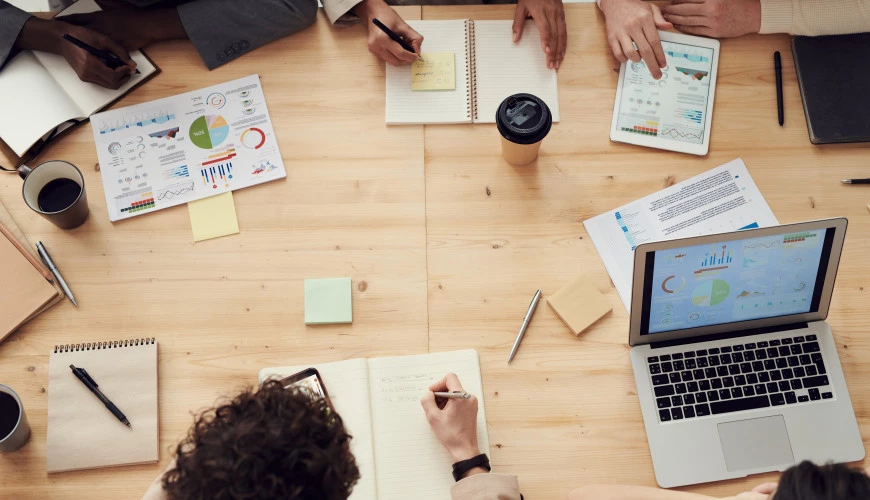 overhead of people working together at a table with paper and computers