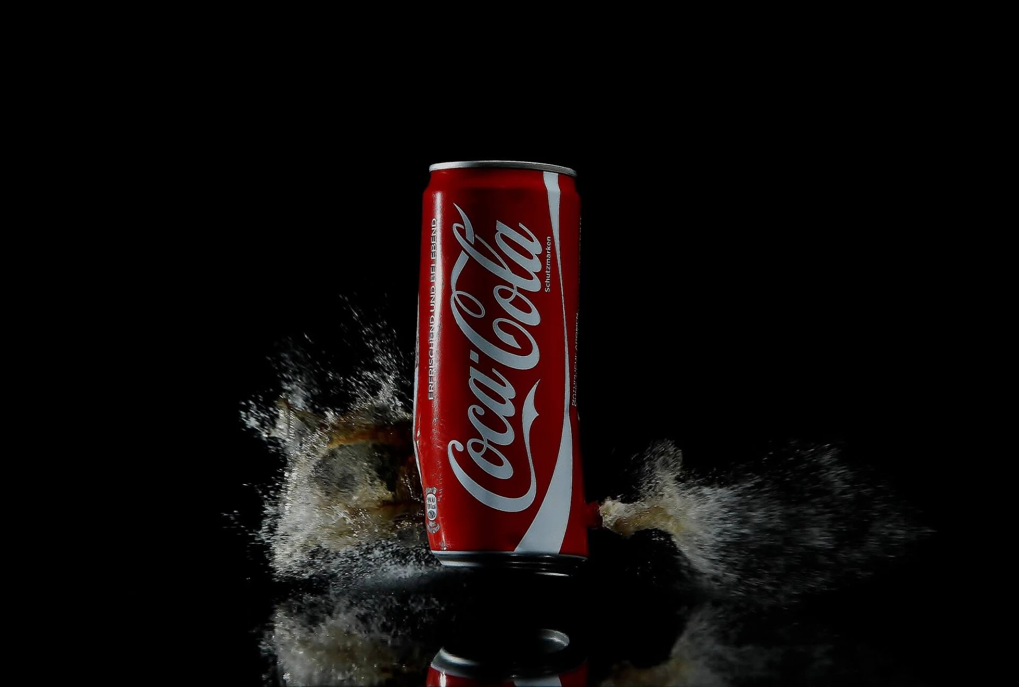 Black background with Coke can in the middle and coke spraying out the bottom.