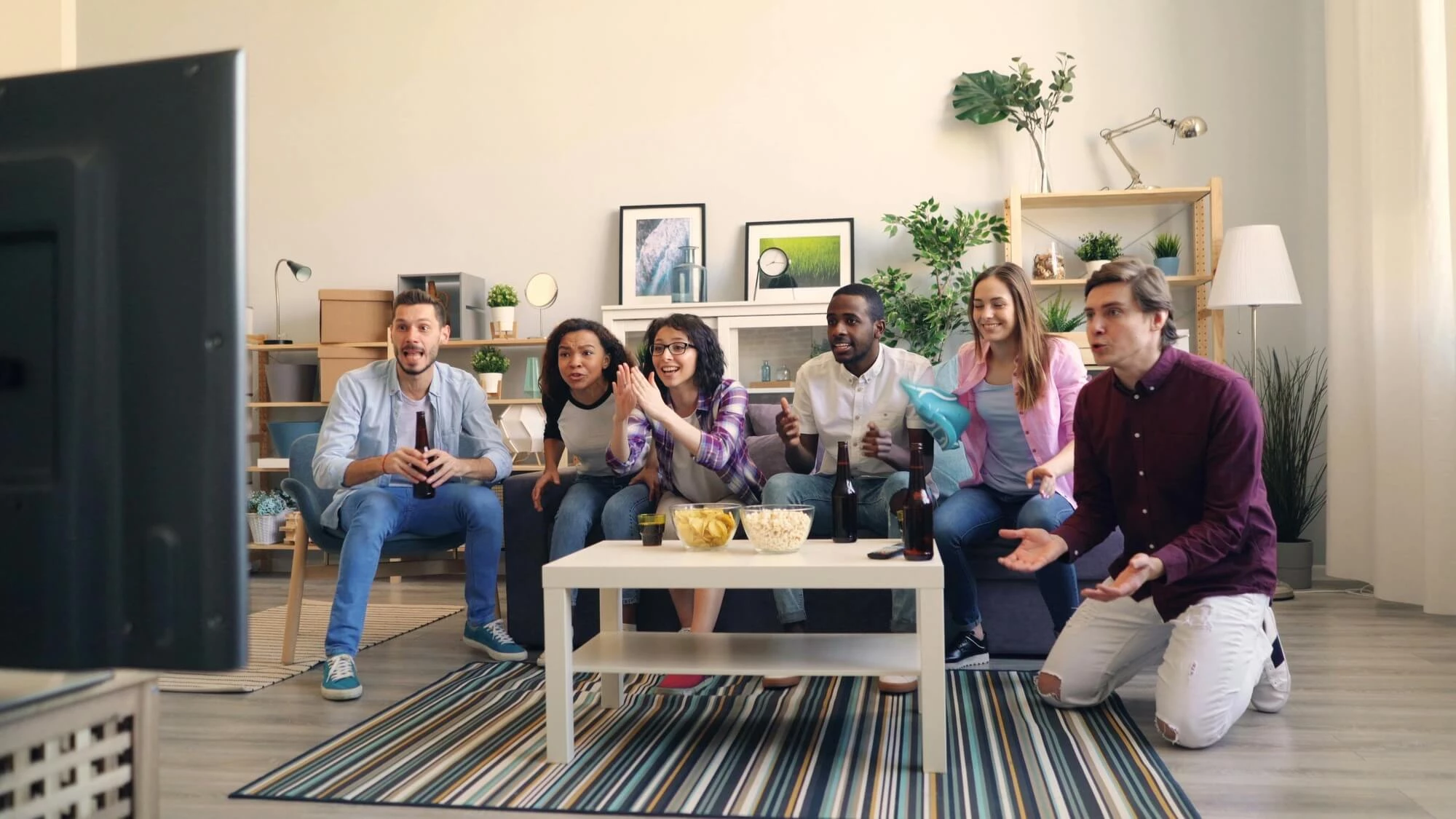 Group of friends with snacks watching a large screen tv.