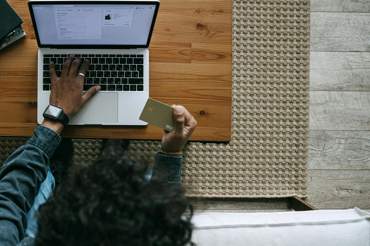 overhead view of a man typing on his laptop while holding a credit card.