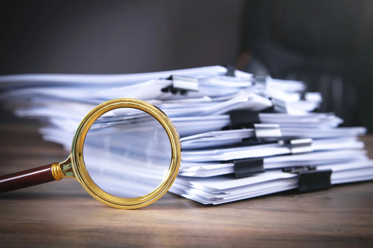 Stack of papers with multiple binder clips and a magnifying glass on it's side.