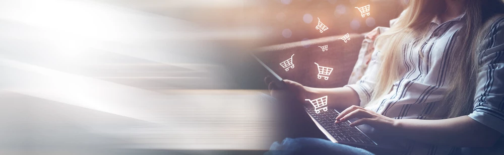 Image of a woman typing on a laptop with small shopping cart icons floating above it.