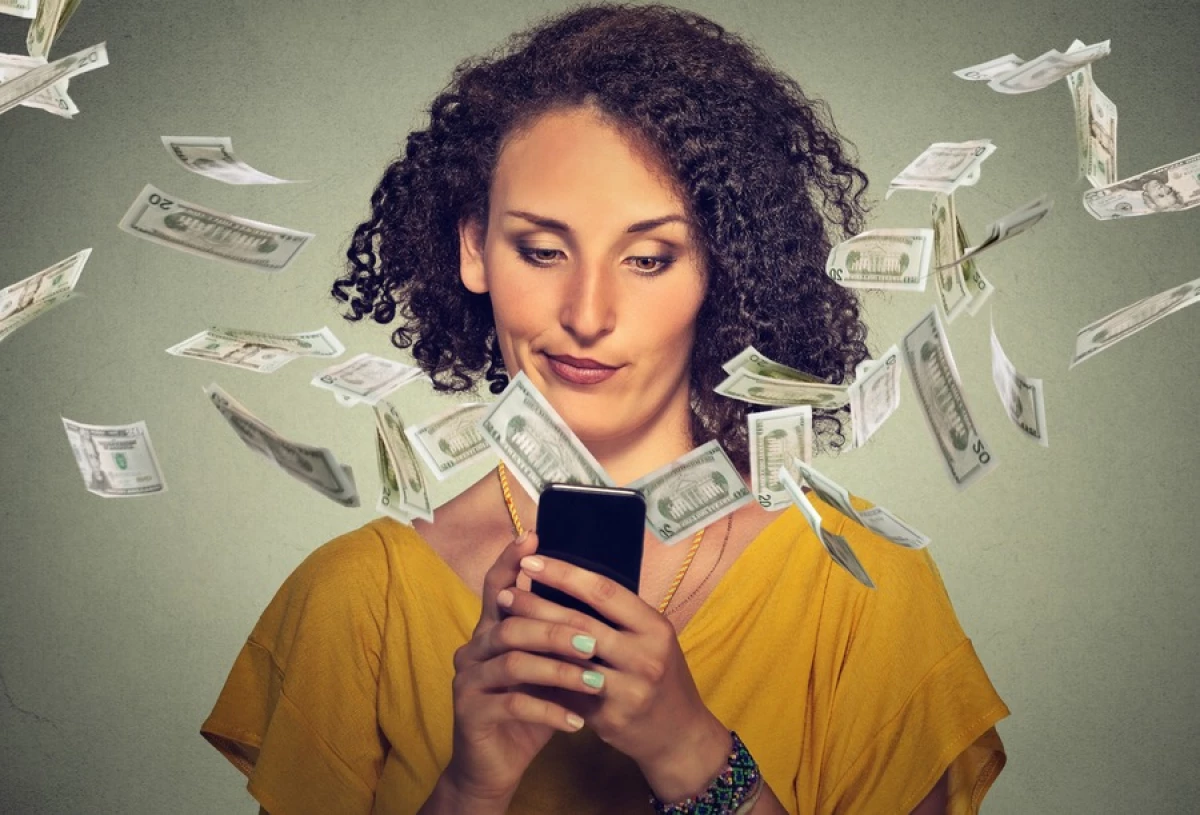 woman looking at phone with money flying around her