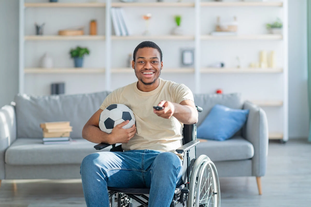 Man in wheelchair holding soccer ball watching TV